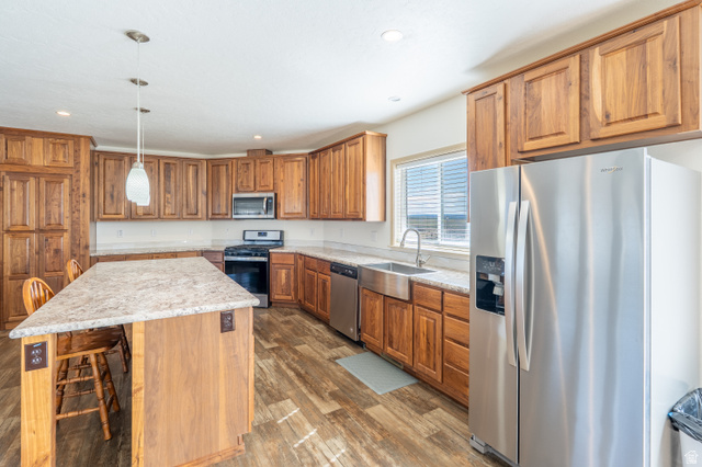 700 East Peter Springs Road Monticello, UT 84535 - Photo 10 of 57 Spacious kitchen featuring an extended island with pendant lighting, ample wood cabinetry, light-toned countertops, stainless steel appliances, and wood-finish flooring