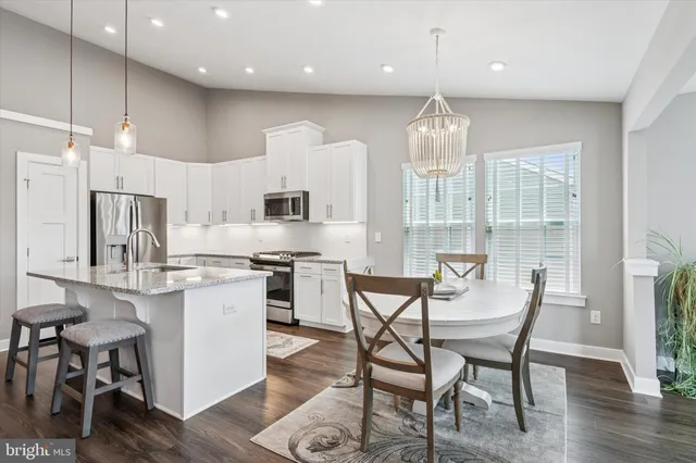 a kitchen with stainless steel appliances kitchen island granite countertop a dining table chairs and white cabinets