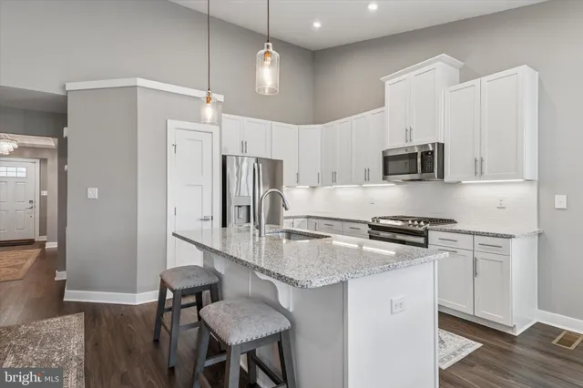 a kitchen with stainless steel appliances granite countertop a stove a refrigerator a sink dishwasher and white cabinets with wooden floor