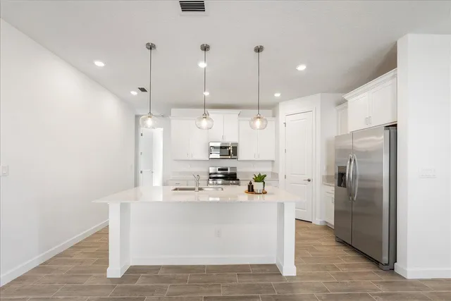 a kitchen with stainless steel appliances a stove a sink a refrigerator a center island and a wooden floor