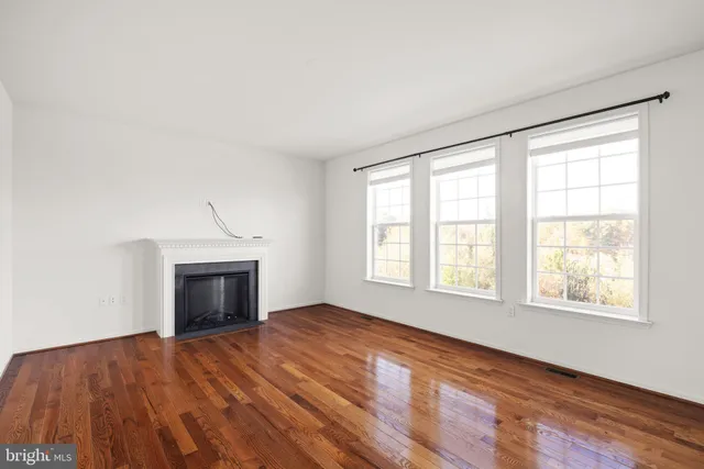 an empty room with windows fireplace and wooden floor