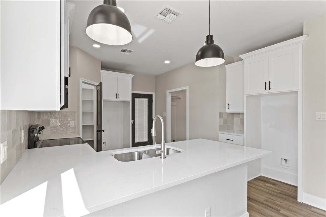 11001-11005 Breedlove Road College Station, TX 77845 - Photo 13 of 40 Kitchen with tasteful backsplash, a peninsula, white cabinetry, light stone countertops, and stove