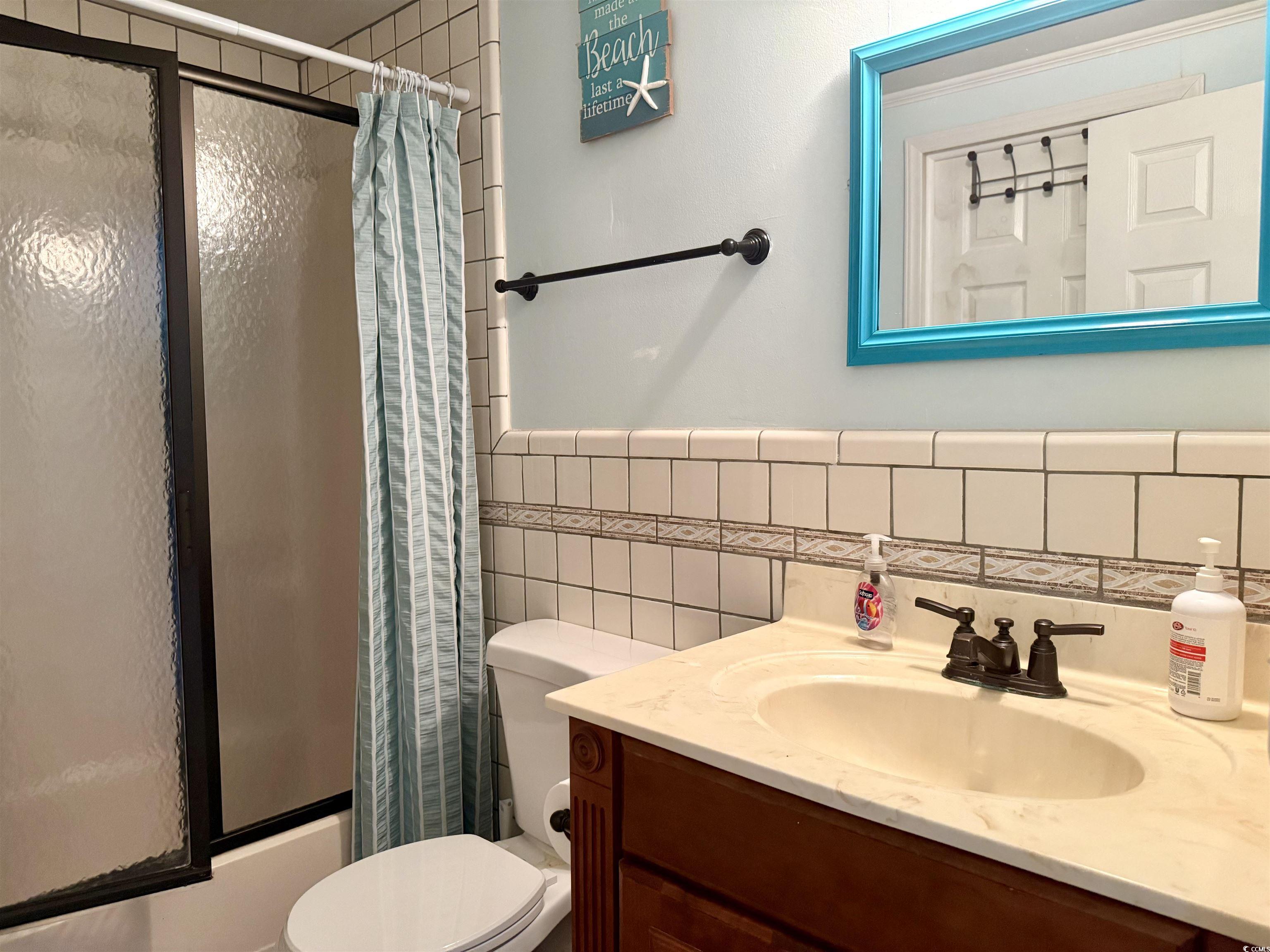 410 E Lake Surfside Beach, SC 29575 - Photo 15 of 27 Bathroom featuring toilet, tile walls, vanity, bath / shower combo with glass door, and a wainscoted wall