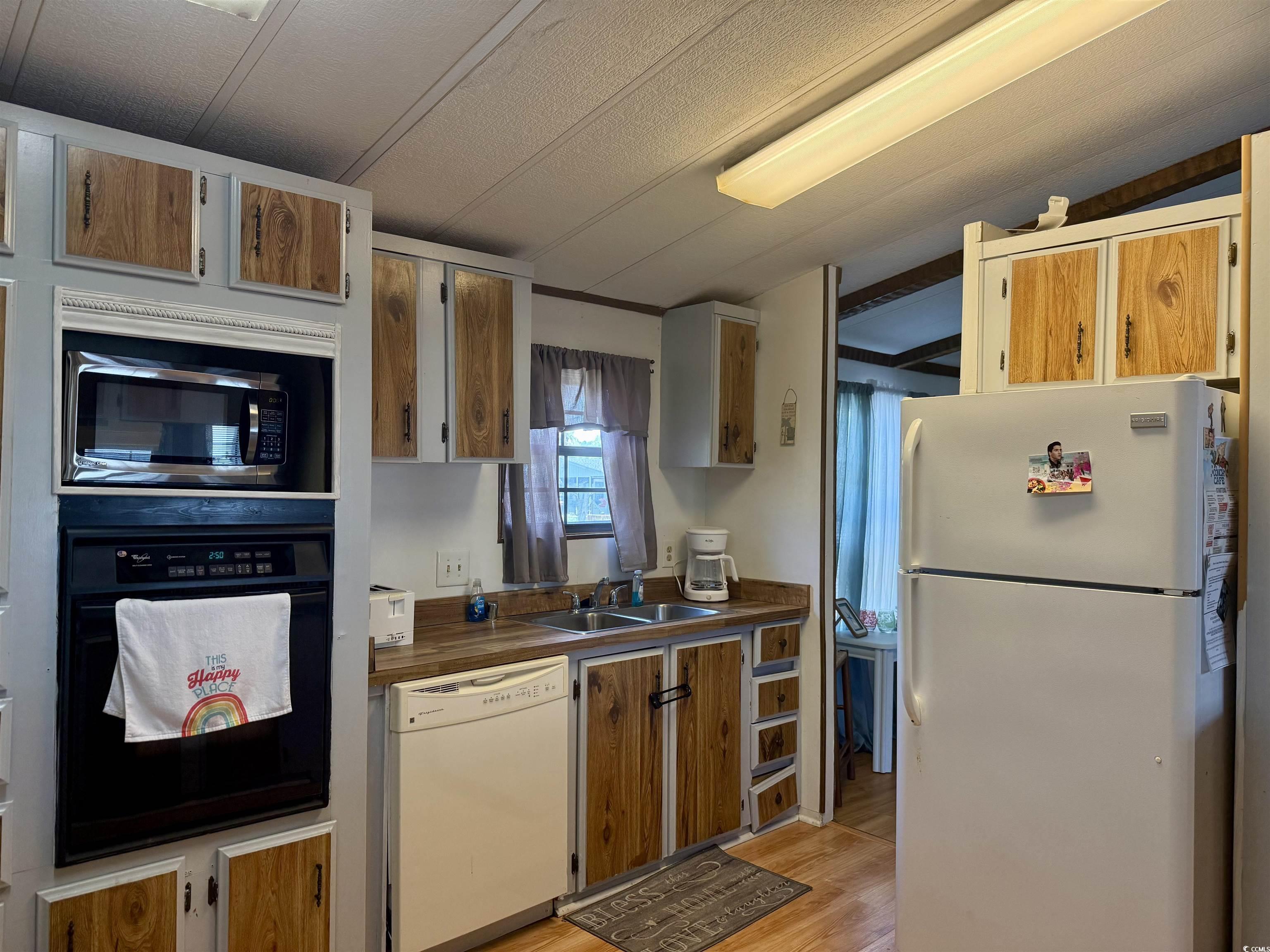 410 E Lake Surfside Beach, SC 29575 - Photo 3 of 27 Kitchen with white appliances, light wood-style floors, dark countertops, a sink, and lofted ceiling