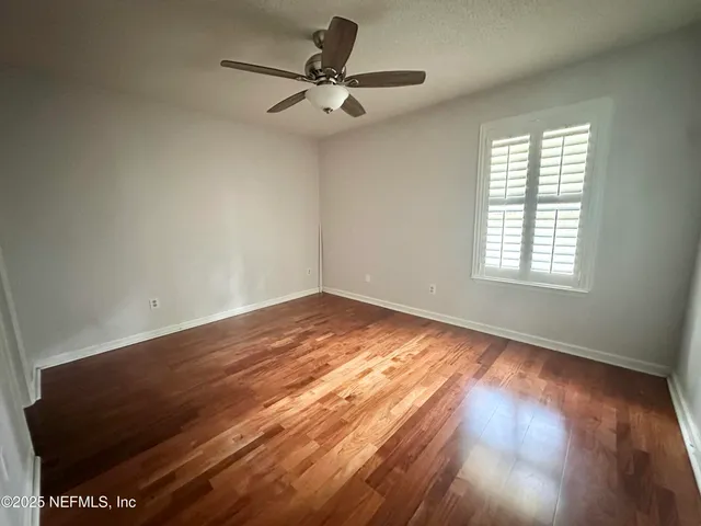 an empty room with wooden floor fan and windows