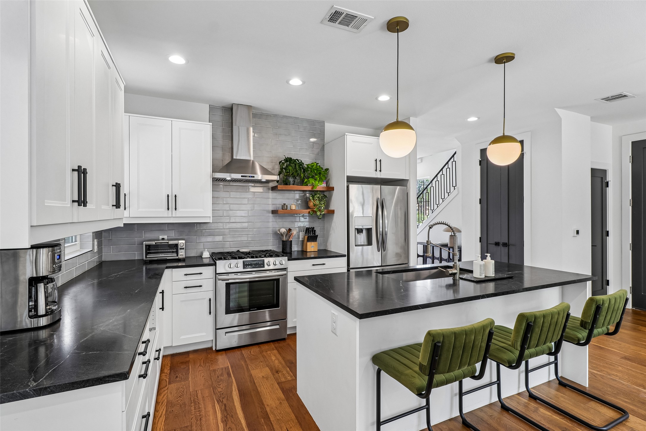 1706 Perez Street, Unit 1 Austin, TX 78721 - Photo 15 of 36 A contemporary kitchen features sleek white cabinetry and rich hardwood flooring, centered around a large island with elegant pendant lighting.