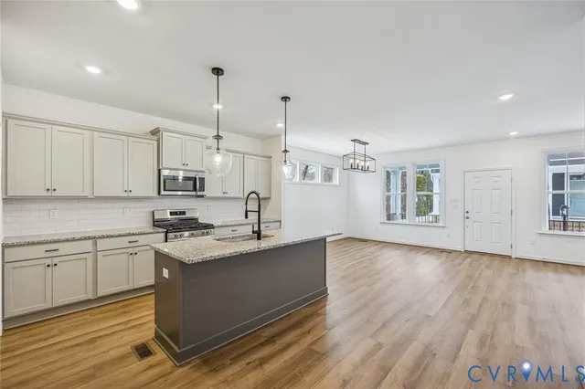 a kitchen with stainless steel appliances granite countertop a sink a stove and white cabinets with wooden floor