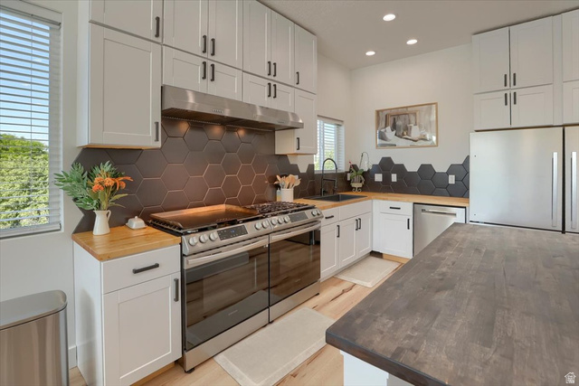 828 South Deer Road Tooele, UT 84074 - Photo 12 of 51 Modern kitchen featuring white shaker-style cabinetry with matte black hardware, hexagonal dark tile backsplash, wood-finish countertops, stainless steel appliances, and recessed lighting