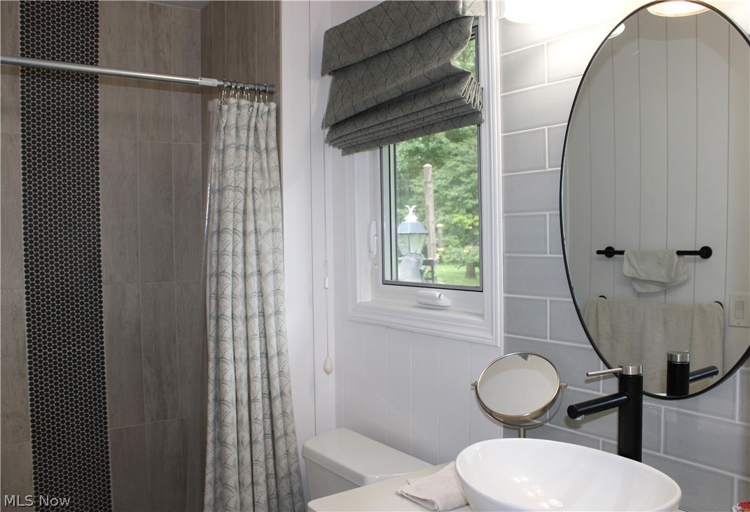 5547 River Styx Road Medina, OH 44256 - Photo 30 of 45 Bathroom featuring a vessel sink with a matte black faucet, subway tile backsplash, and an oval mirror