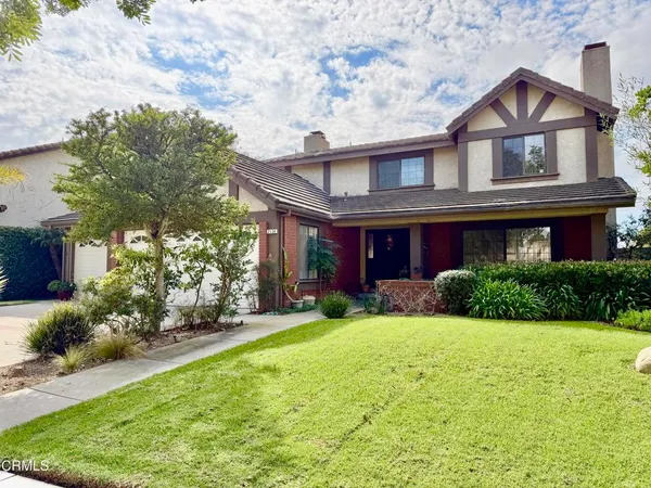 a view of a brick house with a big yard plants and large trees