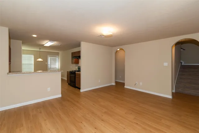 a view of an empty room with wooden floor and kitchen