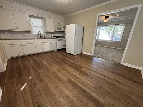 a kitchen with granite countertop a stove a sink and white cabinets with wooden floor