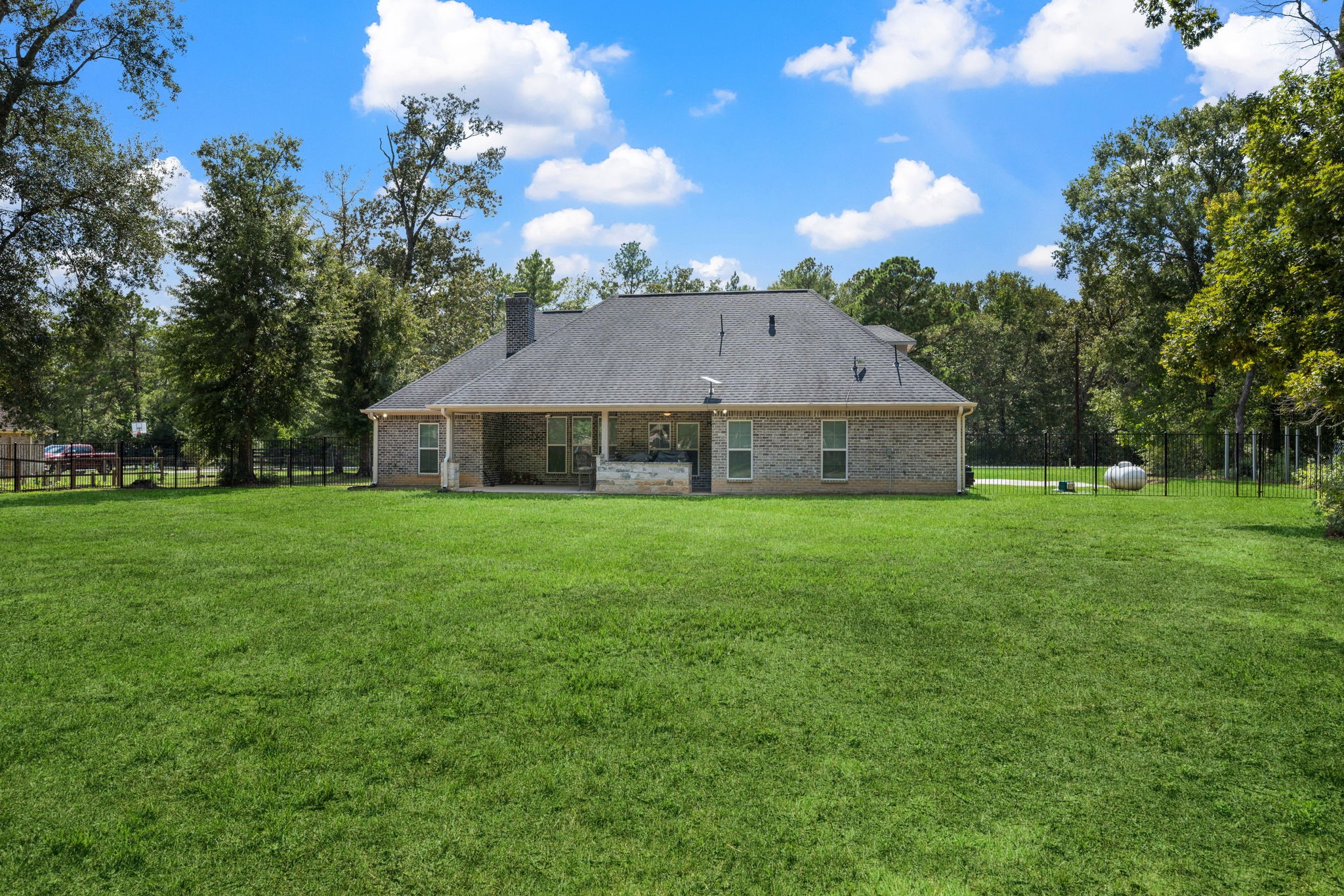 7815 Timber Switch Road Cleveland, TX 77328 - Photo 8 of 39 Expansive backyard offers lush greenery and ample space for outdoor activities, with a charming brick home set against a backdrop of mature trees for added privacy.