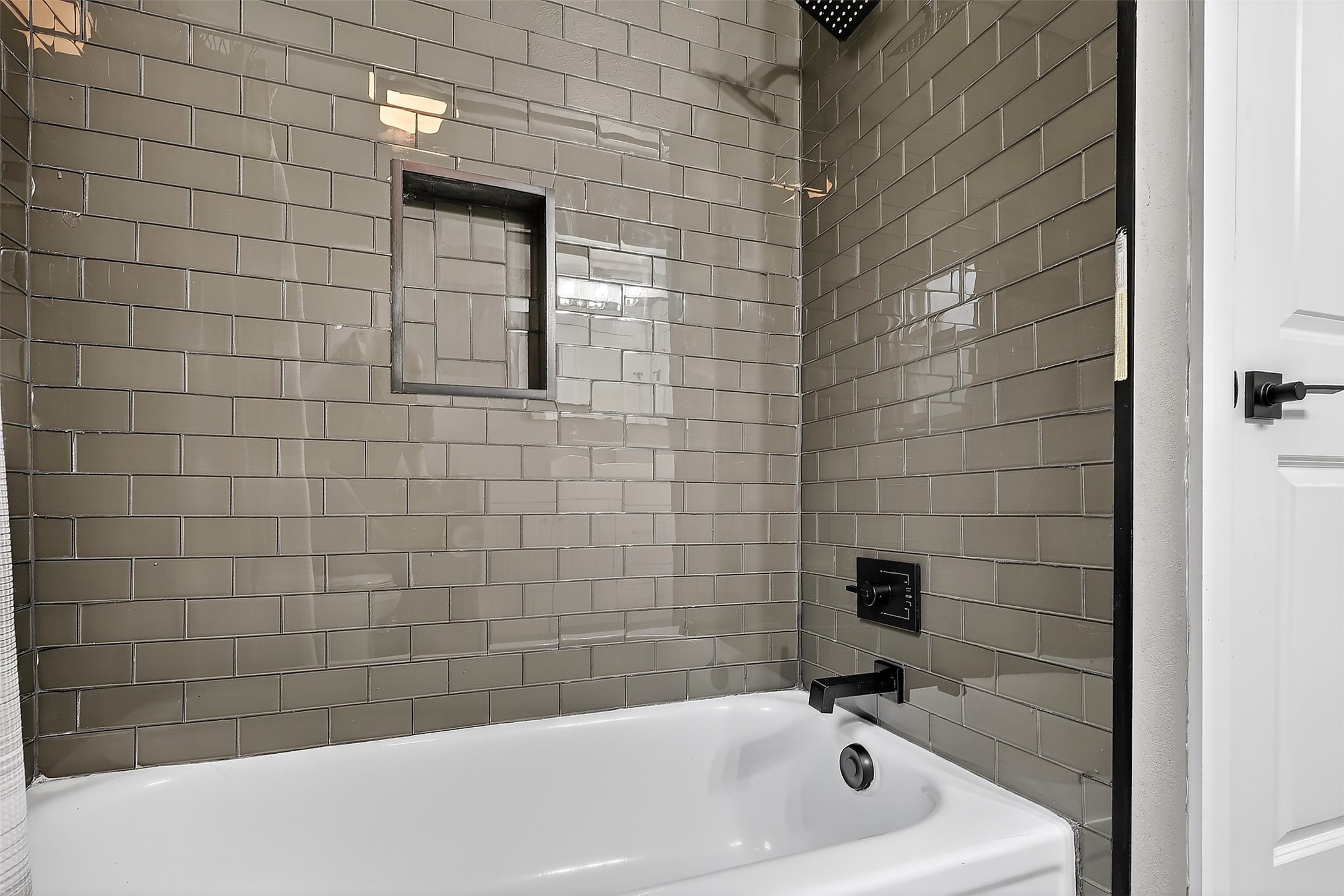 17106 Spring Creek Forest Drive Spring, TX 77379 - Photo 21 of 49 Relax in style within this beautifully updated bathroom featuring floor-to-ceiling glossy taupe subway tile and a built-in recessed niche for a seamless look. The crisp white soaking tub is complemented by sleek matte black hardware, offering a perfect blend of modern design and functional elegance.