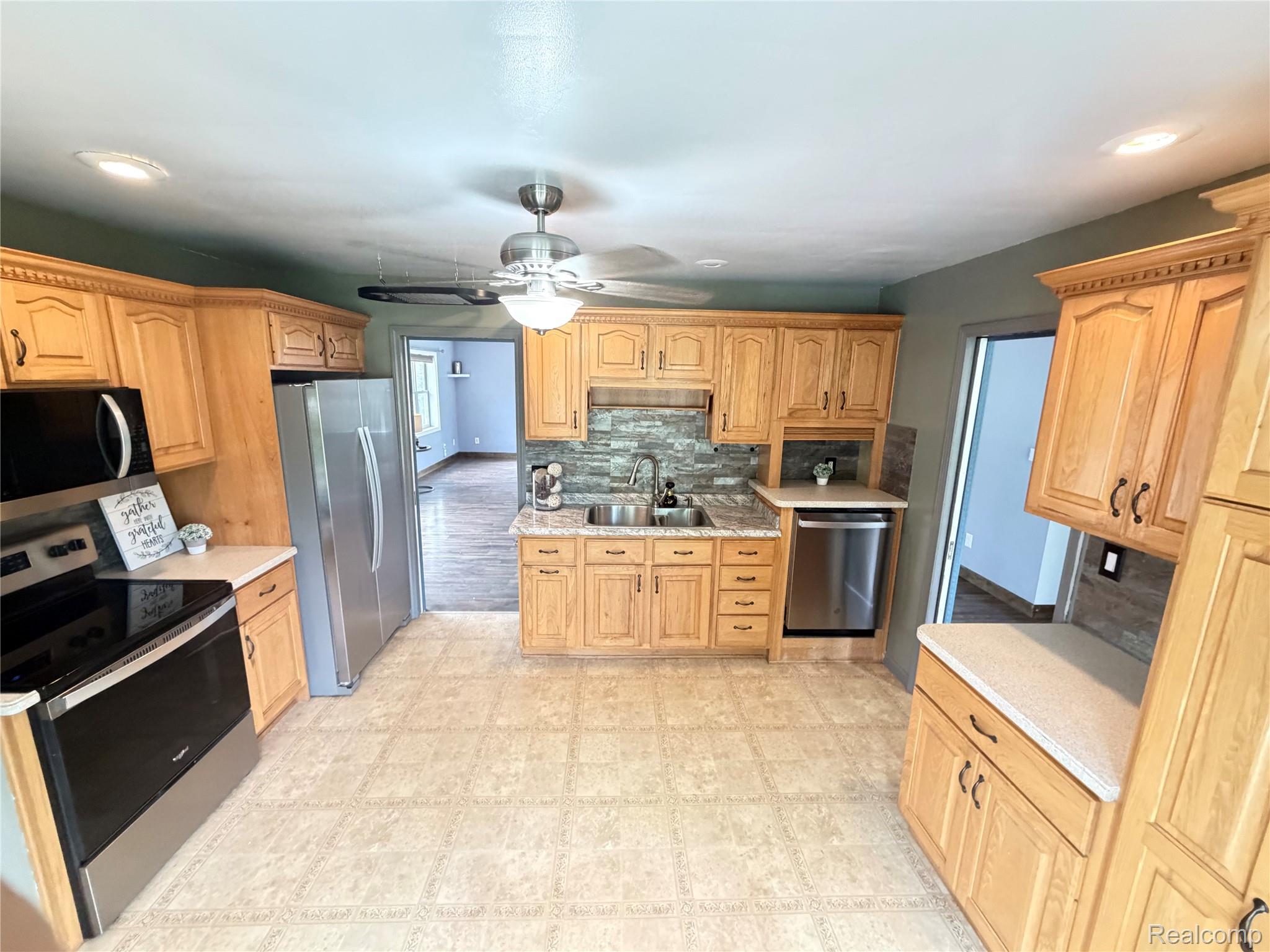 1451 Wilshire Road Haslett, MI 48840 - Photo 18 of 42 Kitchen featuring wood cabinetry, stainless steel appliances, a double basin sink, stone-look backsplash, and textured flooring