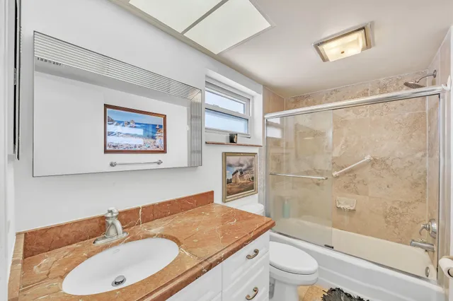 a bathroom with a granite countertop sink a toilet a mirror a vanity a bathtub and shower