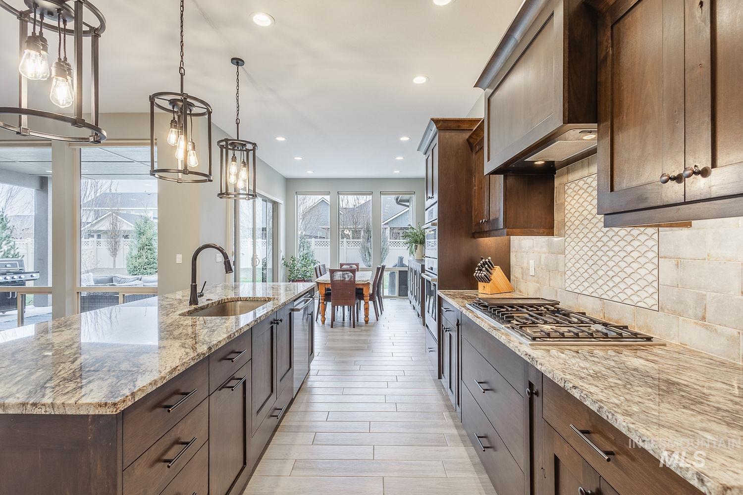 4078 West Wapoot Street Meridian, ID 83646 - Photo 14 of 46 Kitchen with light stone counters, pendant lighting, custom range hood, a large island with sink, and dark brown cabinets