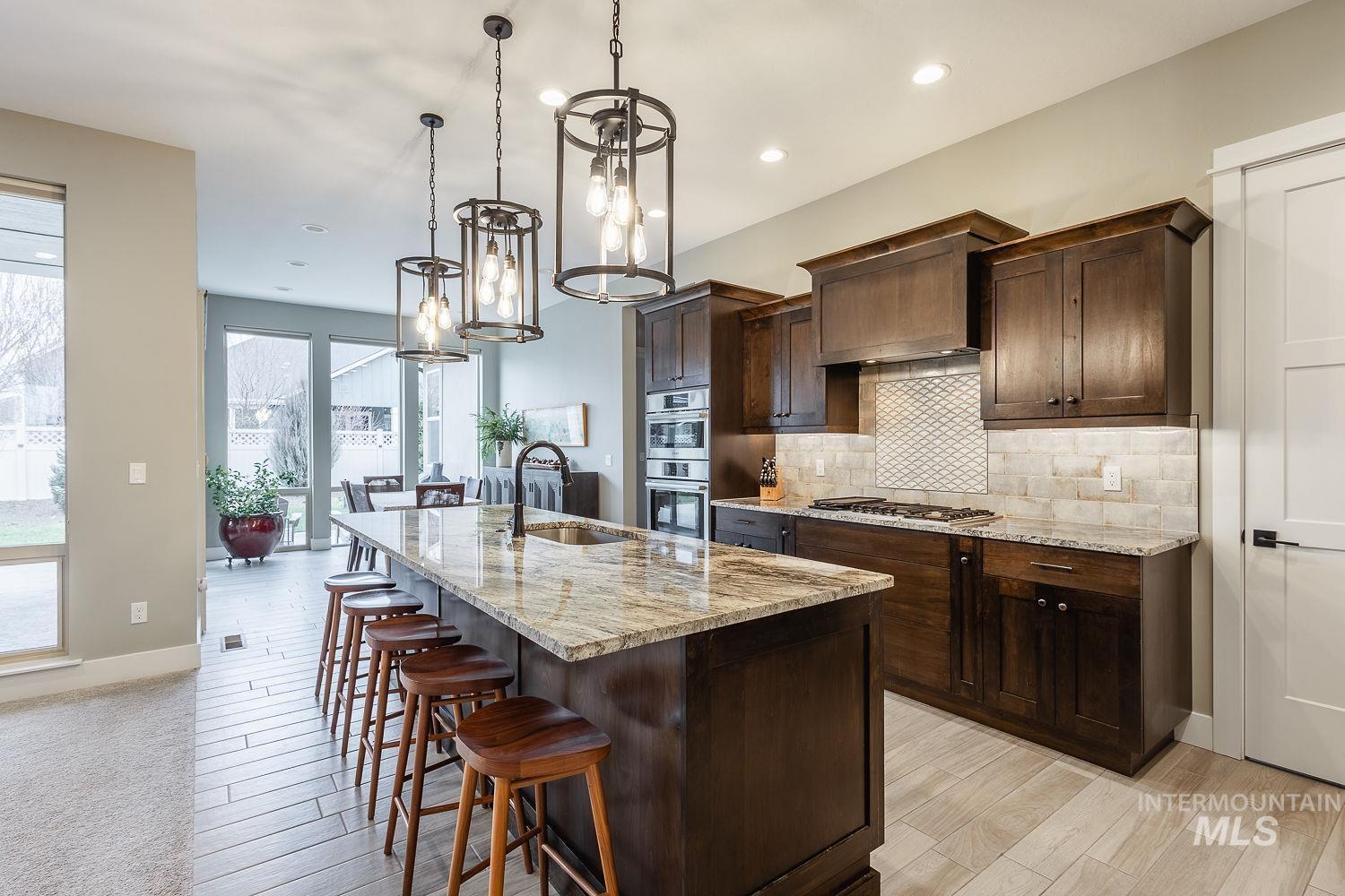 4078 West Wapoot Street Meridian, ID 83646 - Photo 10 of 46 Kitchen with dark brown cabinets, light stone counters, a center island with sink, hanging light fixtures, and light wood-type flooring