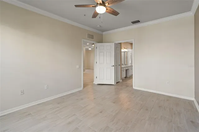 an empty room with chandelier fan and kitchen view