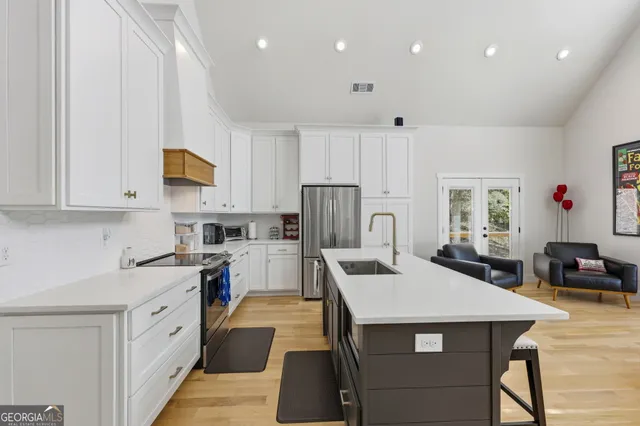 a kitchen with stainless steel appliances granite countertop a stove top oven a sink dishwasher a refrigerator and white cabinets with wooden floor