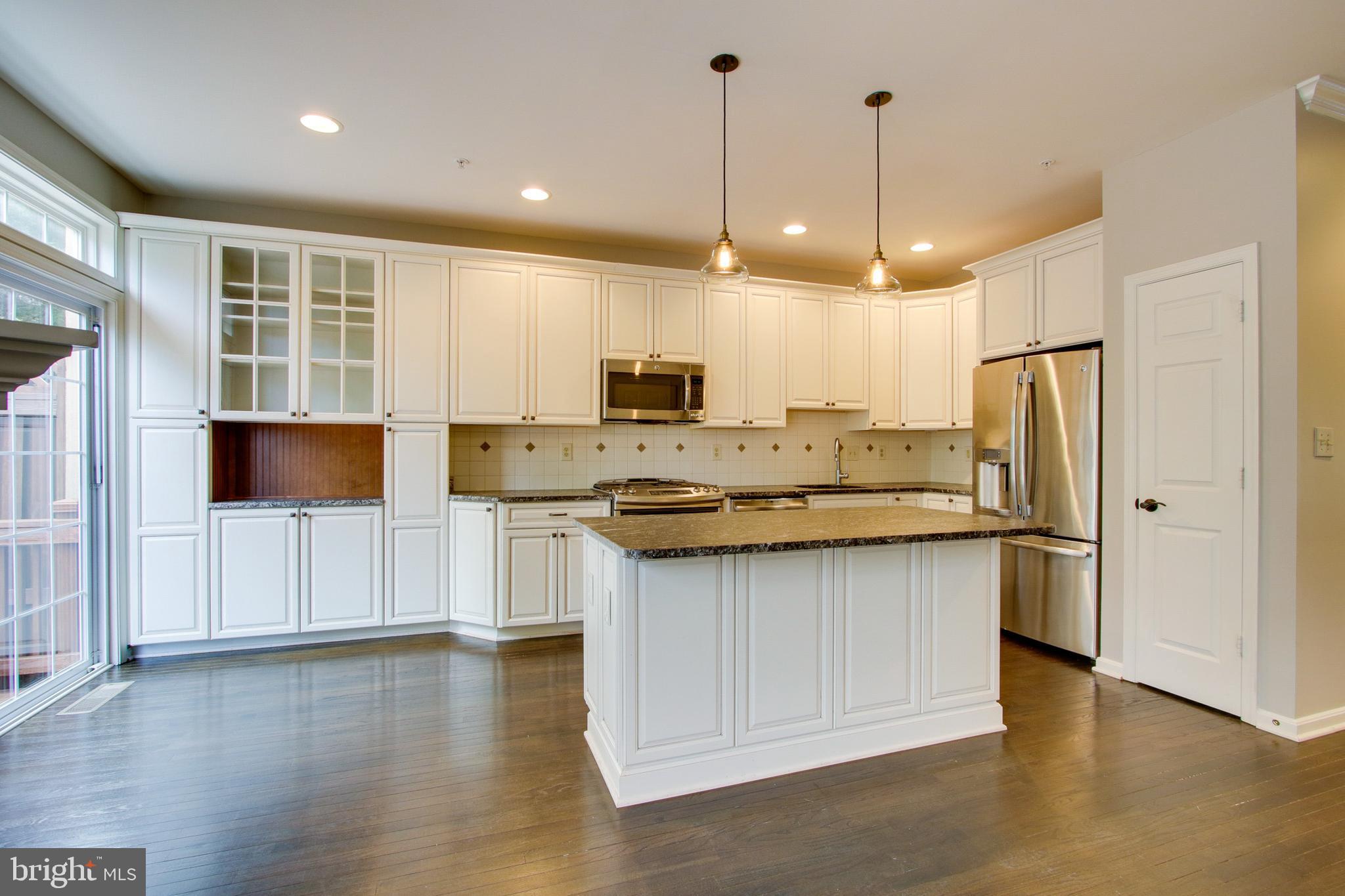 8818 Howard Forest Lane Baltimore, MD 21208 - Photo 9 of 31 a kitchen with stainless steel appliances granite countertop a refrigerator a sink a stove and white cabinets with wooden floor