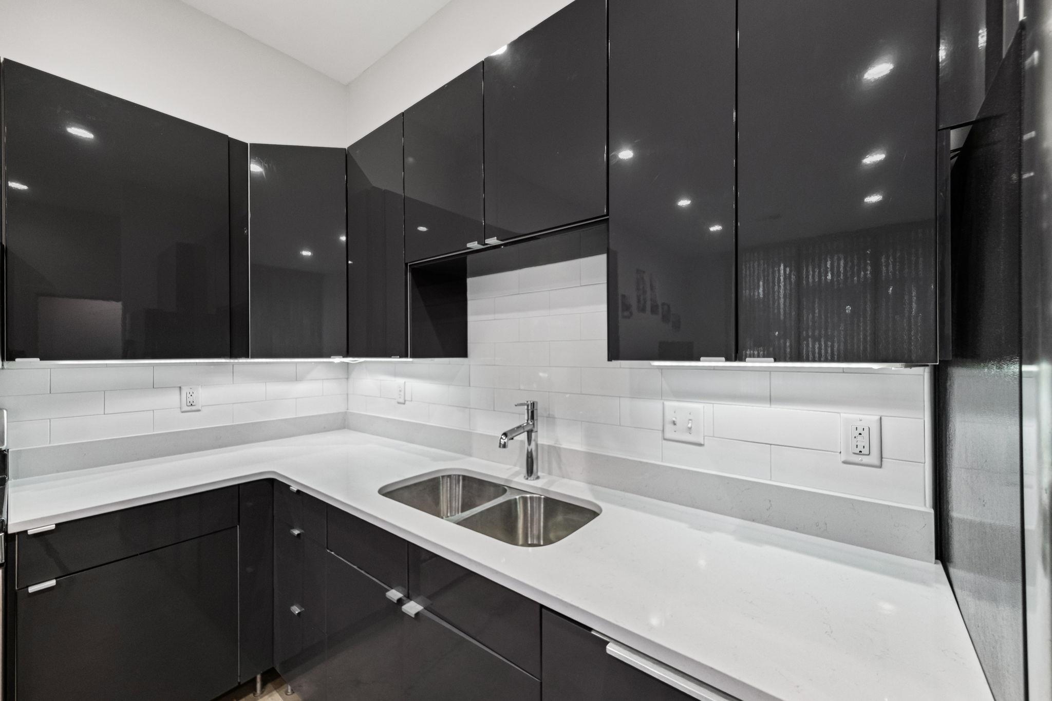 448 Tennessee Street Memphis, TN 38103 - Photo 28 of 39 Contemporary kitchen featuring dark high-gloss cabinetry, light-toned countertops, and a white subway tile backsplash