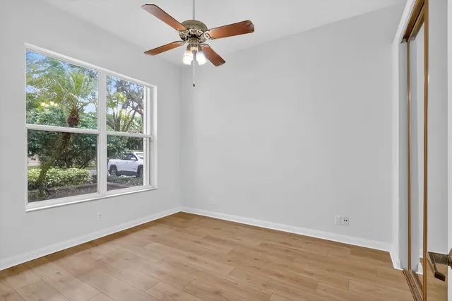an empty room with wooden floor fan and windows