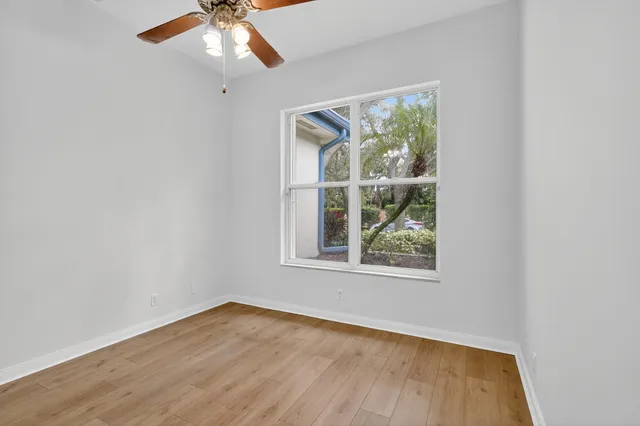 an empty room with wooden floor fan and windows