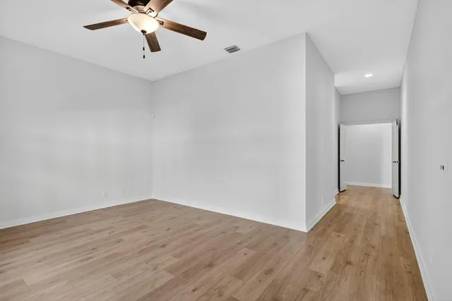an empty room with wooden floor fan and windows