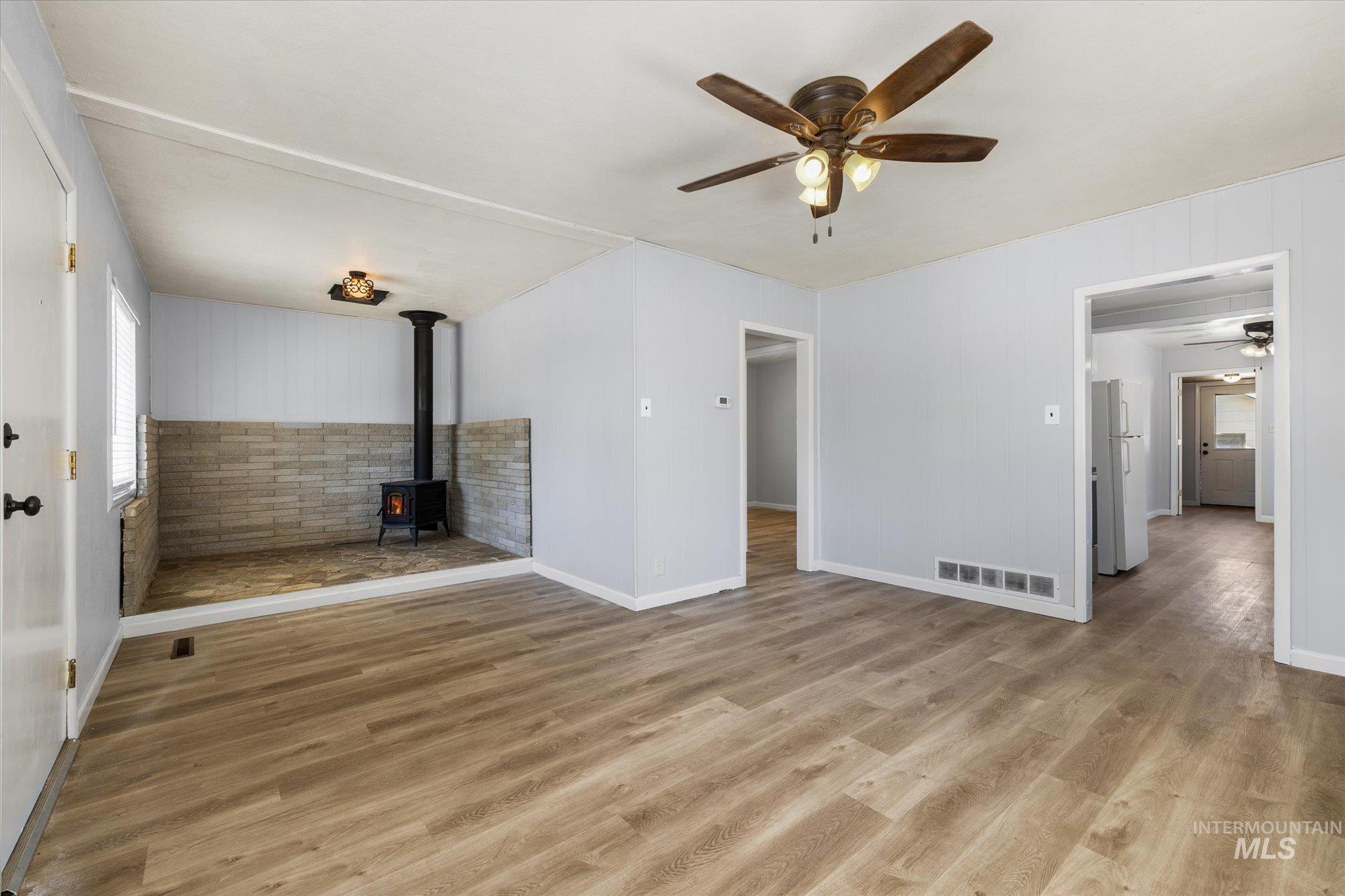 918 West 3rd Street Weiser, ID 83672 - Photo 5 of 36 Spacious living area featuring wood-finish flooring, a wood-burning stove with stone surround, a ceiling fan with integrated lighting, and light gray wall finishes