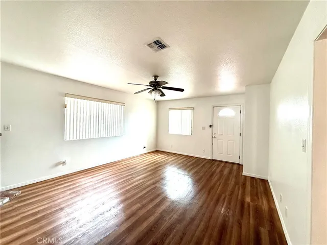an empty room with wooden floor ceiling fan and windows