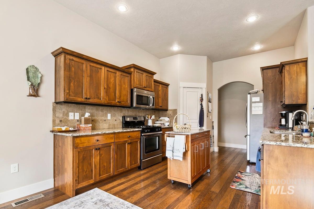 1213 West Lowry Street Meridian, ID 83646 - Photo 17 of 38 Kitchen featuring arched walkways, stainless steel appliances, light stone counters, and wood finish cabinetry