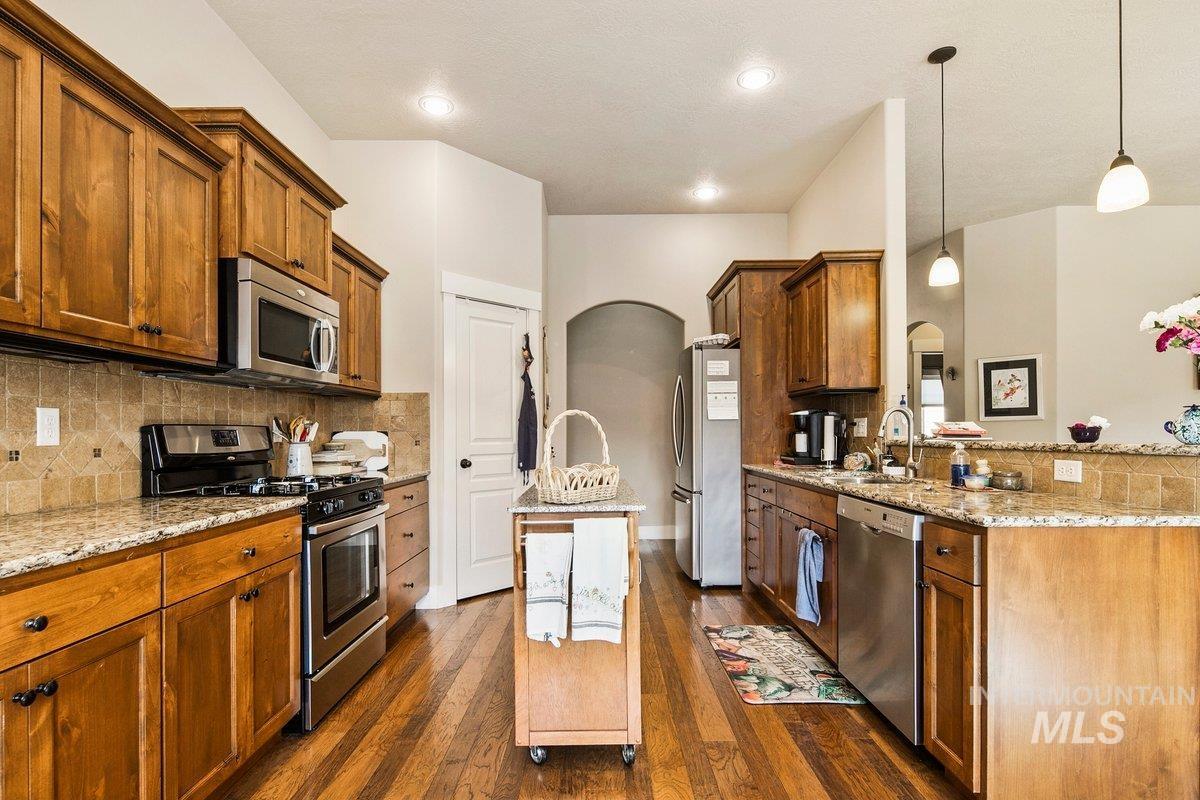 1213 West Lowry Street Meridian, ID 83646 - Photo 18 of 38 Kitchen featuring stainless steel appliances, hanging light fixtures, light stone countertops, arched walkways, and dark wood finished floors