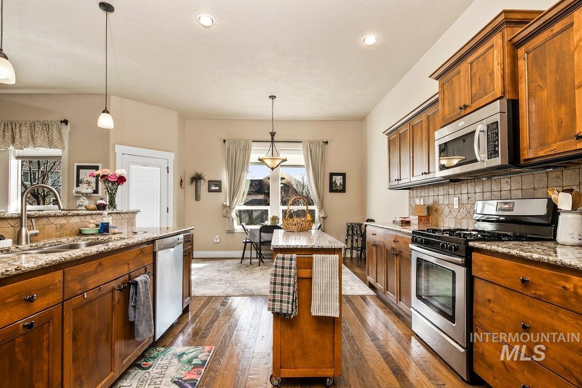 1213 West Lowry Street Meridian, ID 83646 - Photo 20 of 38 Kitchen featuring tasteful backsplash, stainless steel appliances, light stone countertops, decorative light fixtures, and wood finish cabinetry