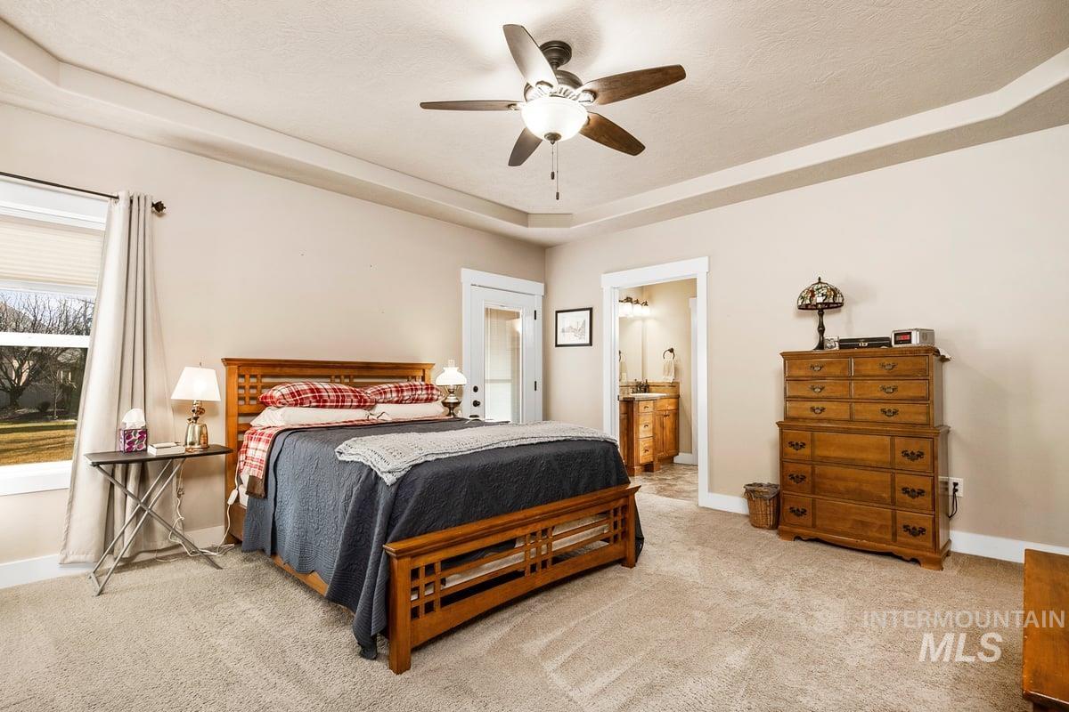 1213 West Lowry Street Meridian, ID 83646 - Photo 21 of 38 Bedroom featuring a ceiling fan, light carpet, connected bathroom, a tray ceiling, and a textured ceiling