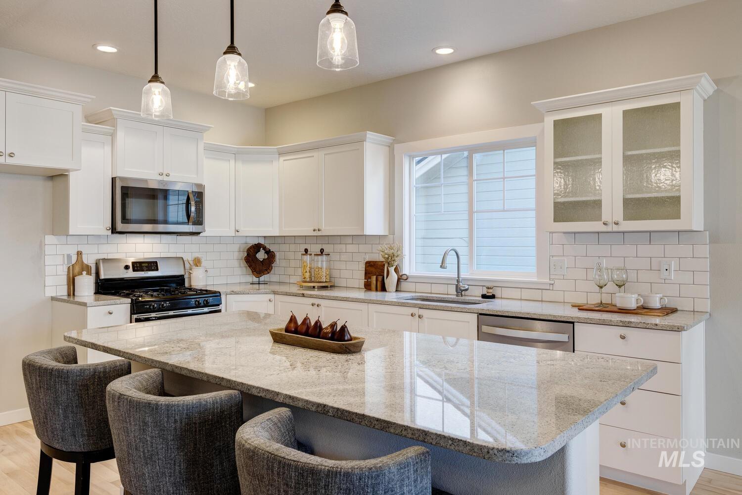 5572 West School Ridge Road Boise, ID 83714 - Photo 12 of 50 Kitchen with light wood-style floors, light stone countertops, appliances with stainless steel finishes, a breakfast bar, and white cabinets