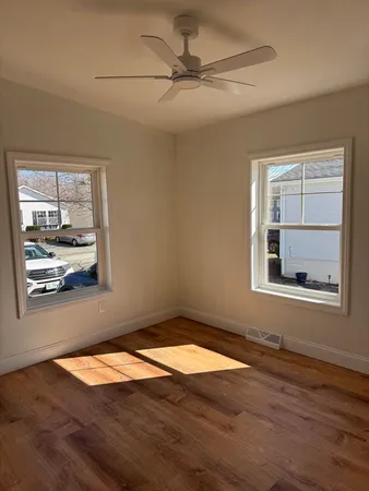 an empty room with wooden floor fan and windows