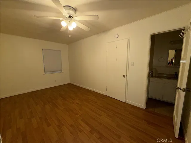 a view of an empty room with wooden floor and a ceiling fan
