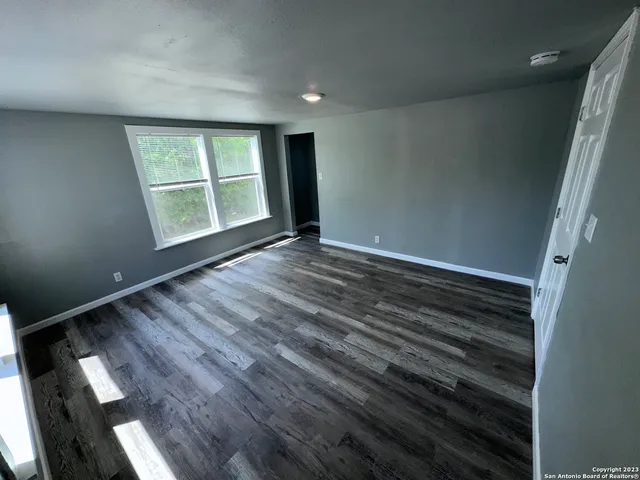 a view of an empty room with wooden floor and a window