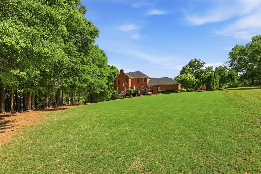 103 5 Knoll Court Anderson, SC 29621 - Photo 27 of 33 A verdant lawn unfolds toward a stately brick residence, framed by mature trees under a clear sky.