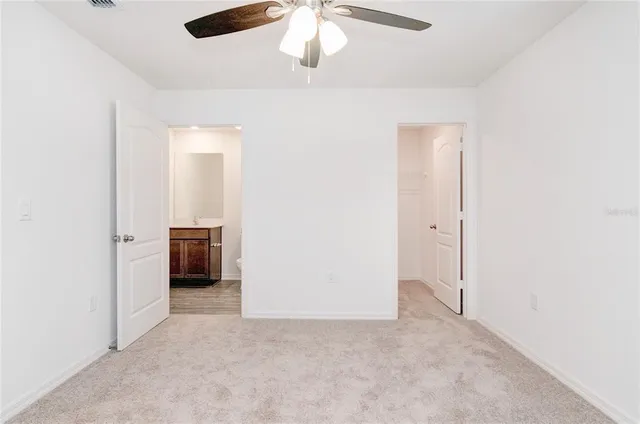 an empty room with a ceiling fan and kitchen view