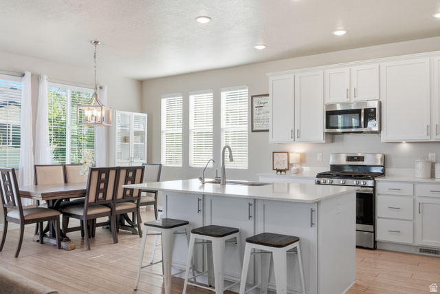 3244 West 1670th Street North Provo, UT 84601 - Photo 12 of 56 Open-concept kitchen and dining area featuring a central island with integrated sink, stainless steel appliances, white cabinetry, and wood-finish flooring