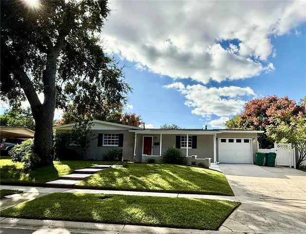 a view of a white house next to a yard with potted plants and large trees