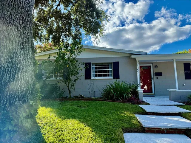 a view of a house with a yard plants and large tree