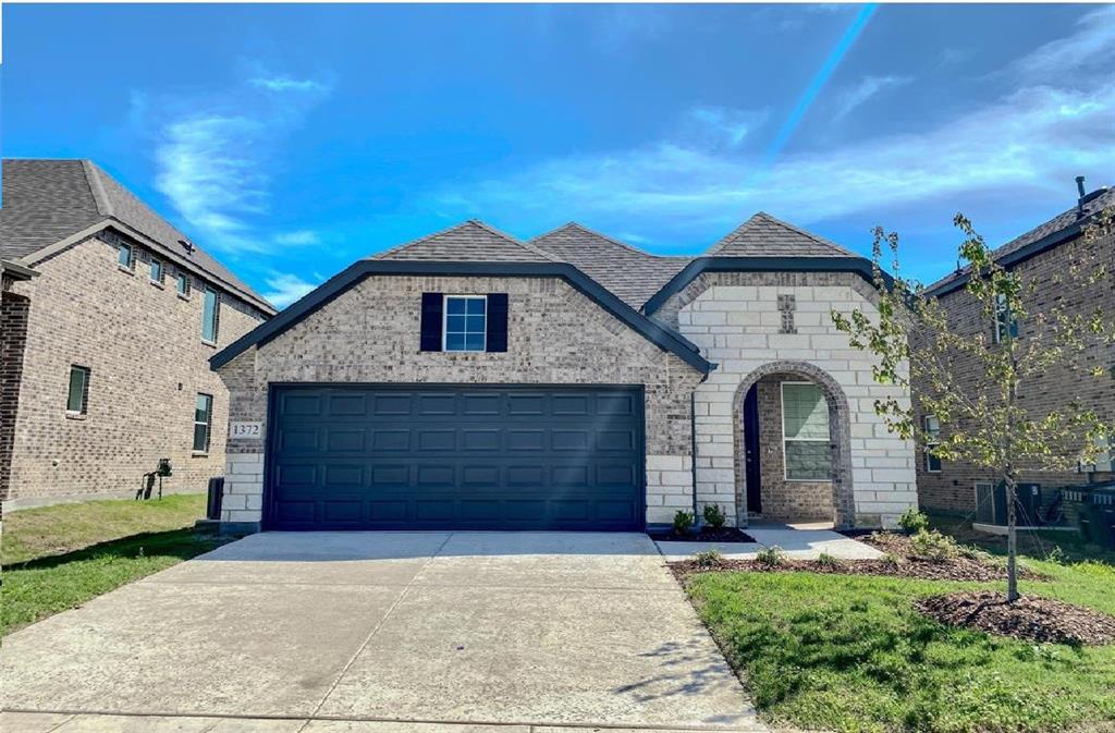 French country style house with brick siding, concrete driveway, stone siding, an attached garage, and roof with shingles
