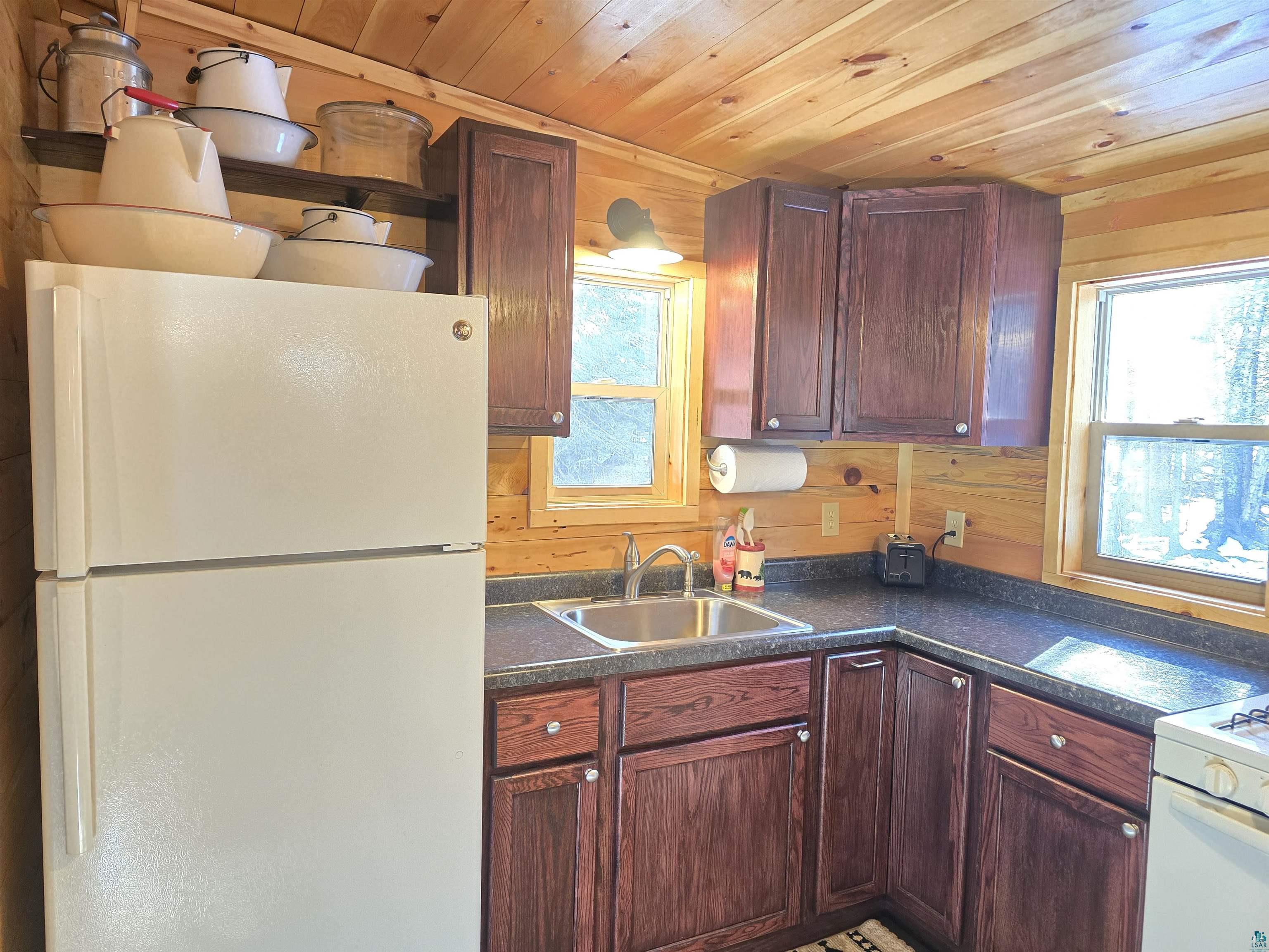 88910 Bark Point Road Herbster, WI 54844 - Photo 16 of 31 Kitchen featuring wooden ceiling, white appliances, wood walls, a sink, and dark countertops