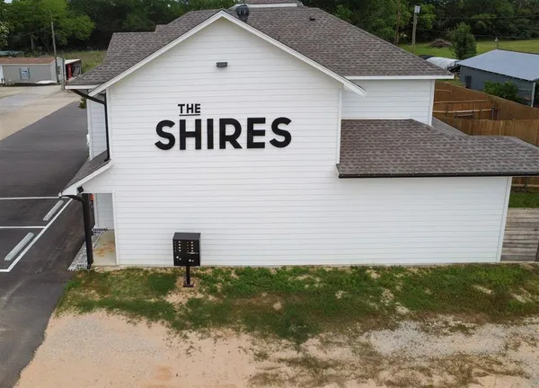 a view of a white house next to a yard with plants and large trees