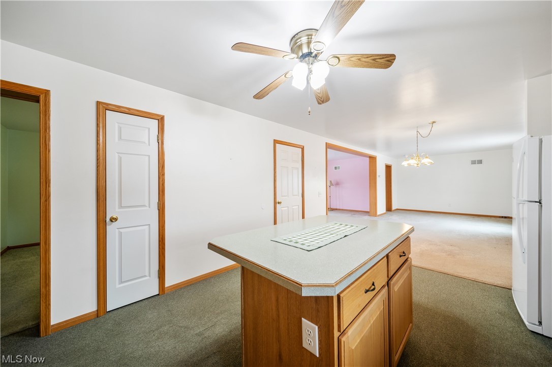 6037 Gerald Road Ashtabula, OH 44004 - Photo 10 of 34 Kitchen with white refrigerator, ceiling fan with notable chandelier, a kitchen island, and dark colored carpet