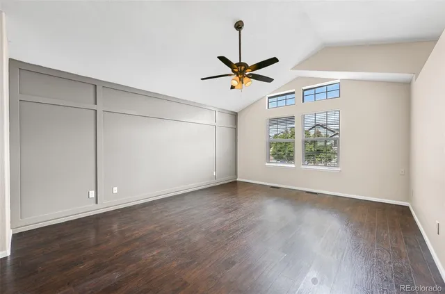 an empty room with wooden floor ceiling fan and windows