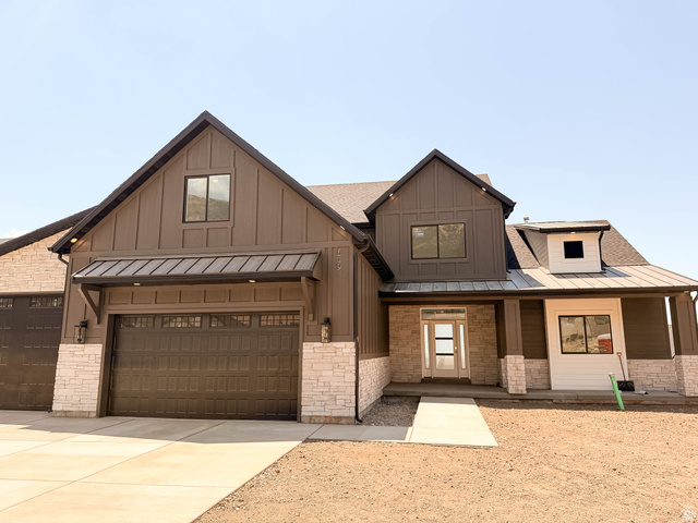 Modern farmhouse exterior featuring board and batten siding, stone accents, a metal awning, an attached two-car garage, and a covered porch with a dormer